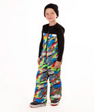A child wearing a black knit beanie, a black long-sleeve top, and colorful camo print snow bib overalls, standing against a plain white background.