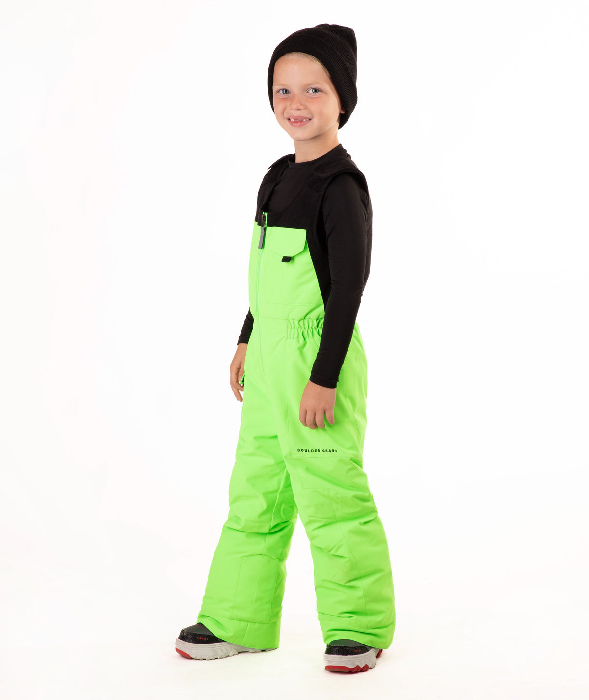 A child wearing bright neon green snow bib overalls over a black long-sleeve shirt and black beanie, standing against a plain white studio background.