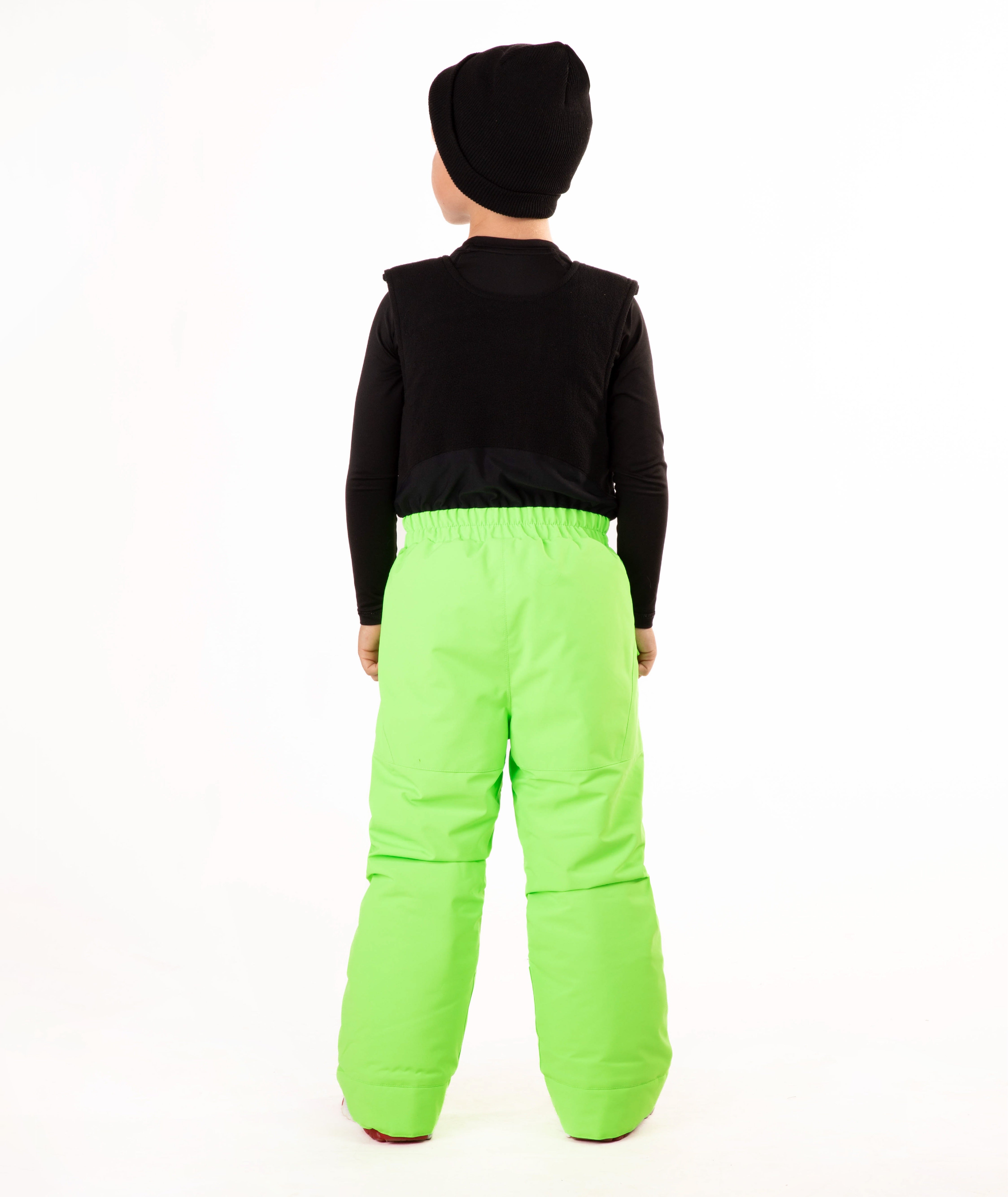 A child wearing bright neon green snow bib overalls over a black long-sleeve shirt and black beanie, standing against a plain white studio background.