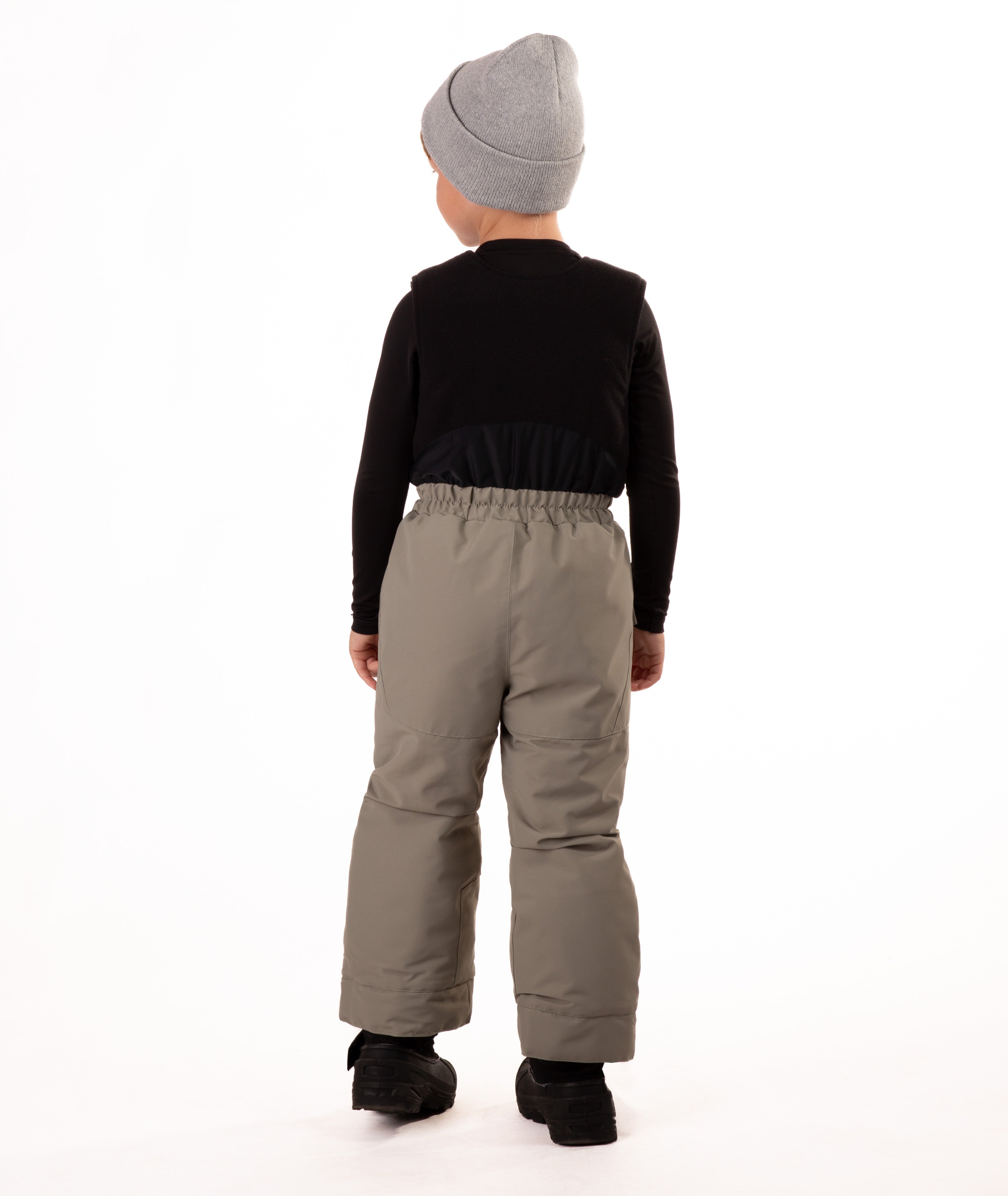 Child wearing beige snow bibs on a white background showing back of bib