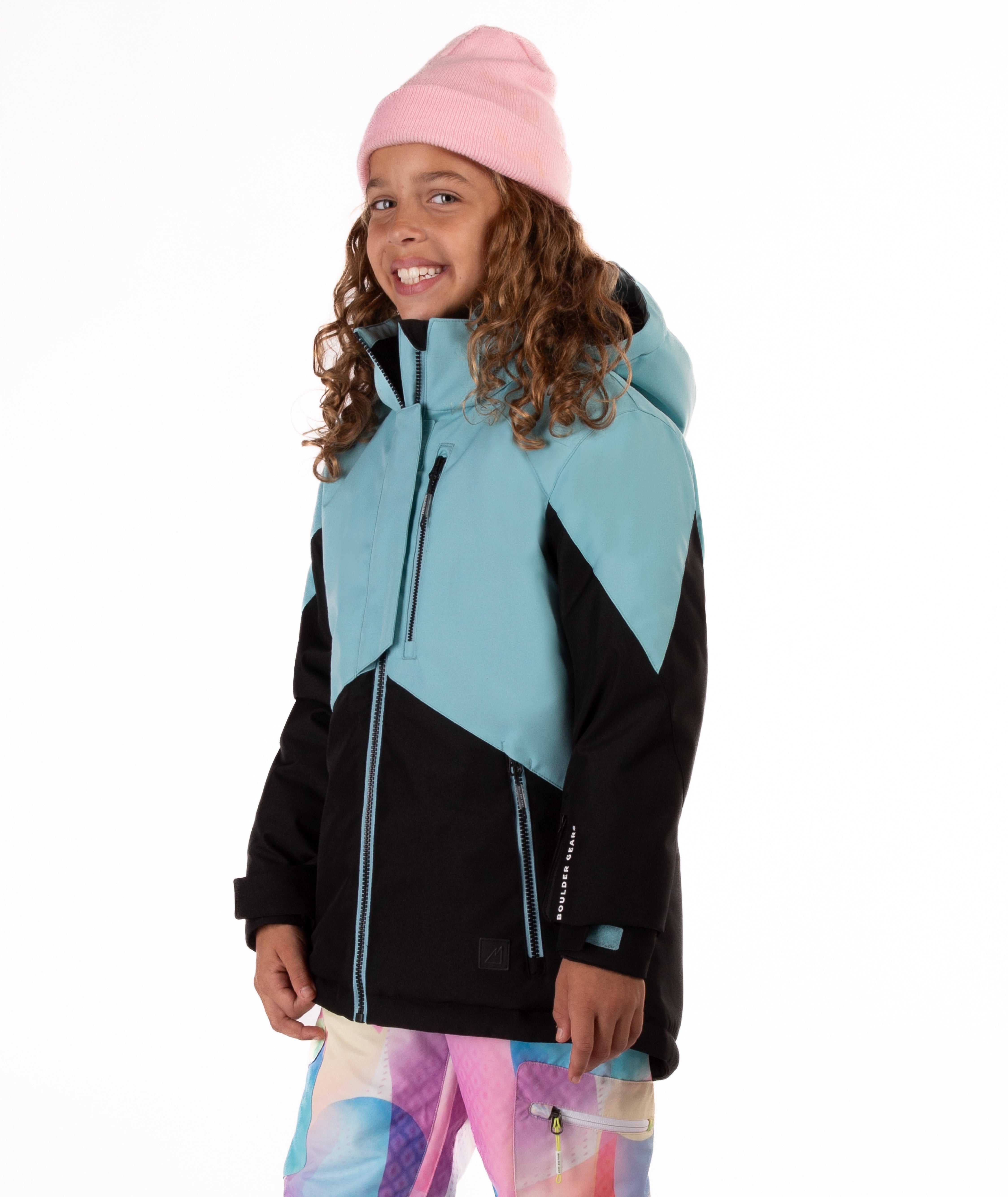 Youth girl wearing a teal and black jacket with contrast zippers on a white background