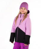 A young girl wearing a lavender and black color-blocked ski jacket, a matching purple beanie, and purple ski pants, photographed against a solid white studio background.
