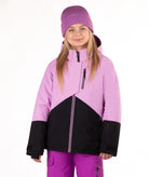 A young girl wearing a lavender and black color-blocked ski jacket, a matching purple beanie, and purple ski pants, photographed against a solid white studio background.