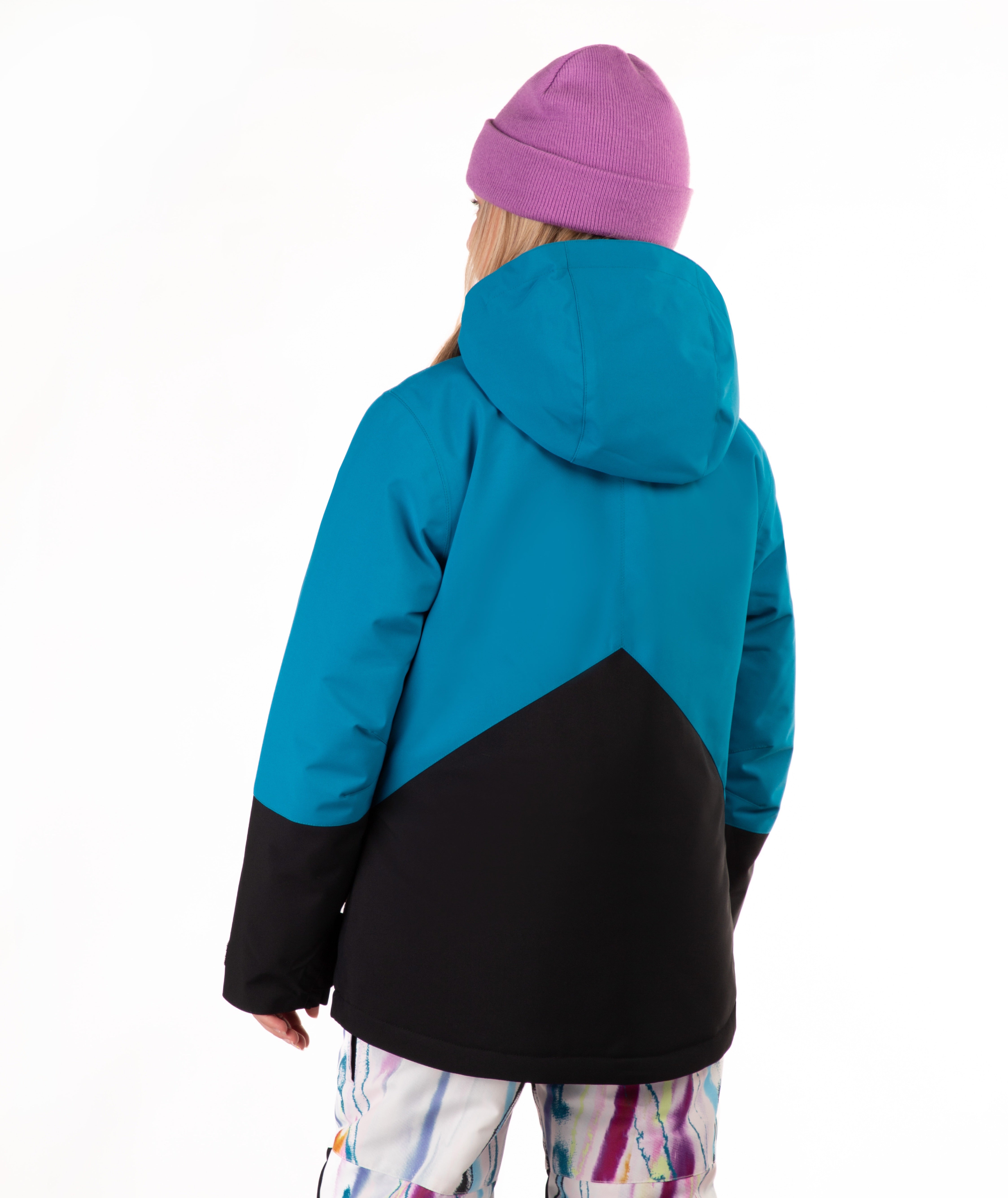 A child shown from the back wearing a color-blocked hooded jacket with a bright teal upper section and black lower section, paired with a purple knit beanie and multicolored patterned pants, against a plain white background.