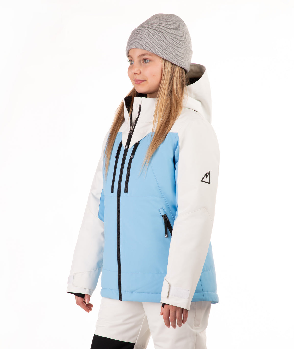 A young girl wearing a light blue and off white color-blocked ski jacket, a gray beanie, and off white ski pants, standing against a solid white background.