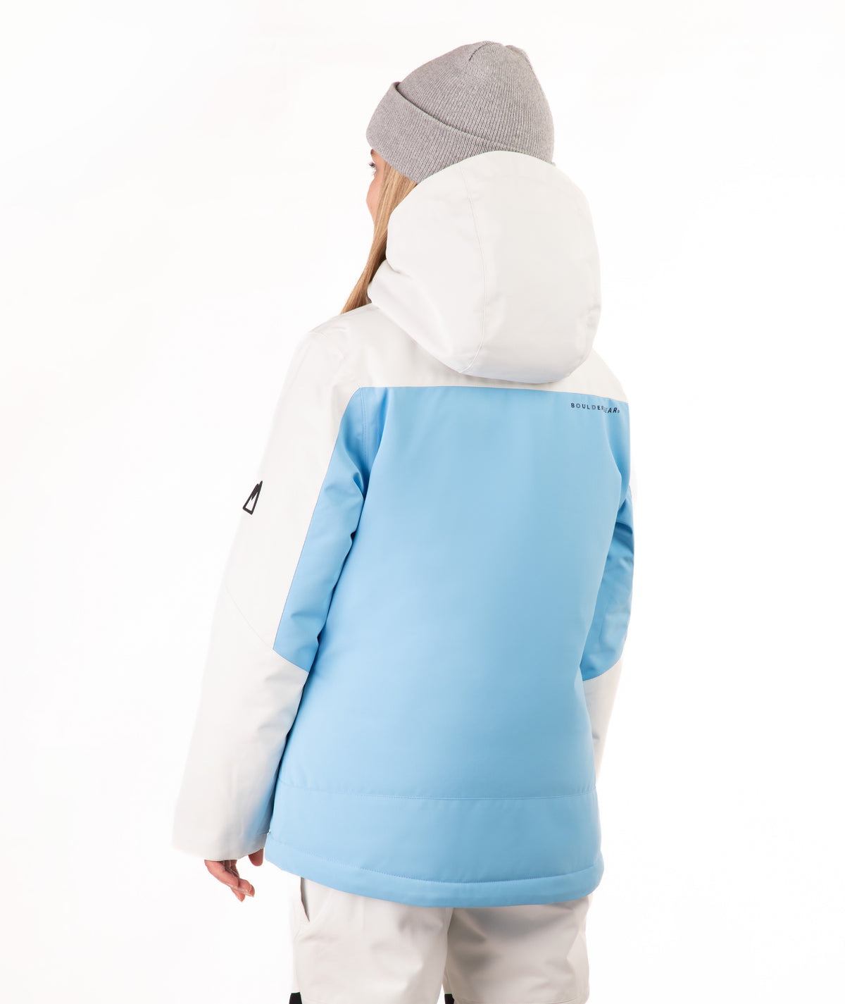 A young girl wearing a light blue and off white color-blocked ski jacket, a gray beanie, and off white ski pants, standing against a solid white background.