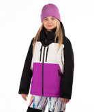 A young girl wearing a color-blocked ski jacket with black sleeves, a white upper chest, and a bright purple lower front panel, paired with a purple beanie and multicolor patterned snow pants, against a plain white background.