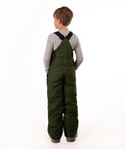 A child viewed from the back wearing dark olive green insulated bib overalls  over a light gray long-sleeve shirt, standing against a plain white studio background.