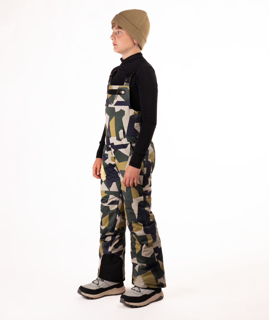 boy wearing camouflage bibs and black top on a white background