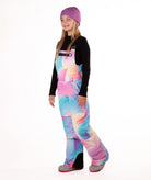girl wearing multi colored abstract pastel pattern snow bibs with a black top on a white background
