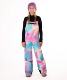 girl wearing multi colored abstract pastel pattern snow bibs with a black top on a white background