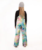A person shown from the back wearing colorful tie-dye snow bibs, a black long-sleeve top, and a gray beanie against a plain white studio background.