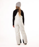 back of girl wearing cream colored snow bibs with a black top on a white background