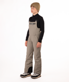 boy wearing beige bibs and black top on a white background