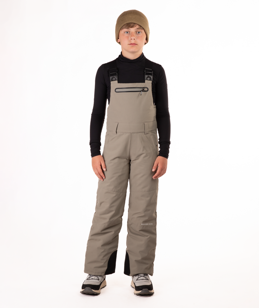 boy wearing beige bibs and black top on a white background