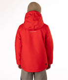 Youth boy wearing a red jacket with a brand logo on the back, standing against a white background