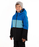 A young boy wearing a color-blocked ski jacket in blue, light blue, and black, paired with a gray beanie, standing against a plain white background.