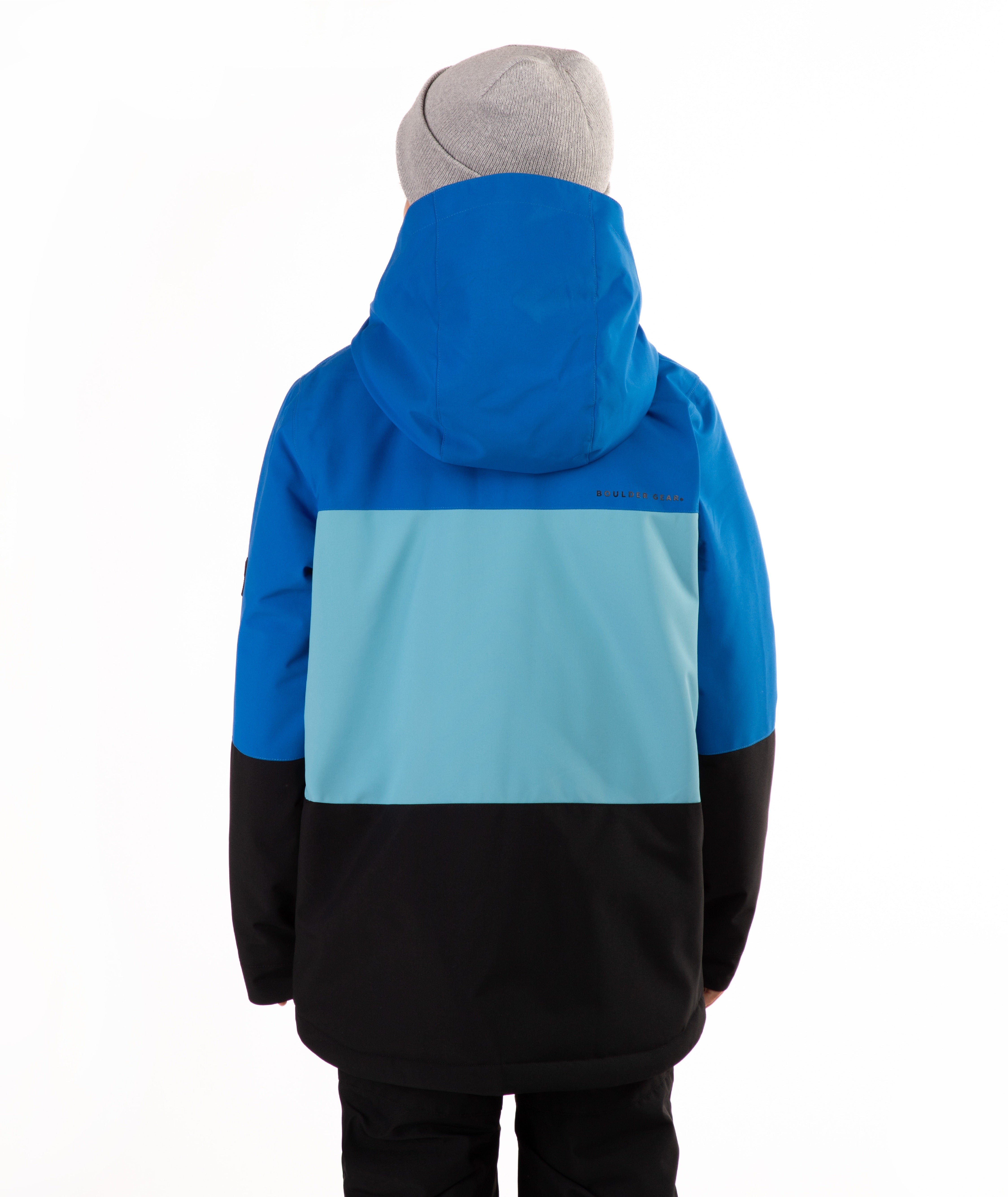 A young boy wearing a color-blocked ski jacket in blue, light blue, and black, paired with a gray beanie, standing against a plain white background.