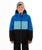 A young boy wearing a color-blocked ski jacket in blue, light blue, and black, paired with a gray beanie, standing against a plain white background.