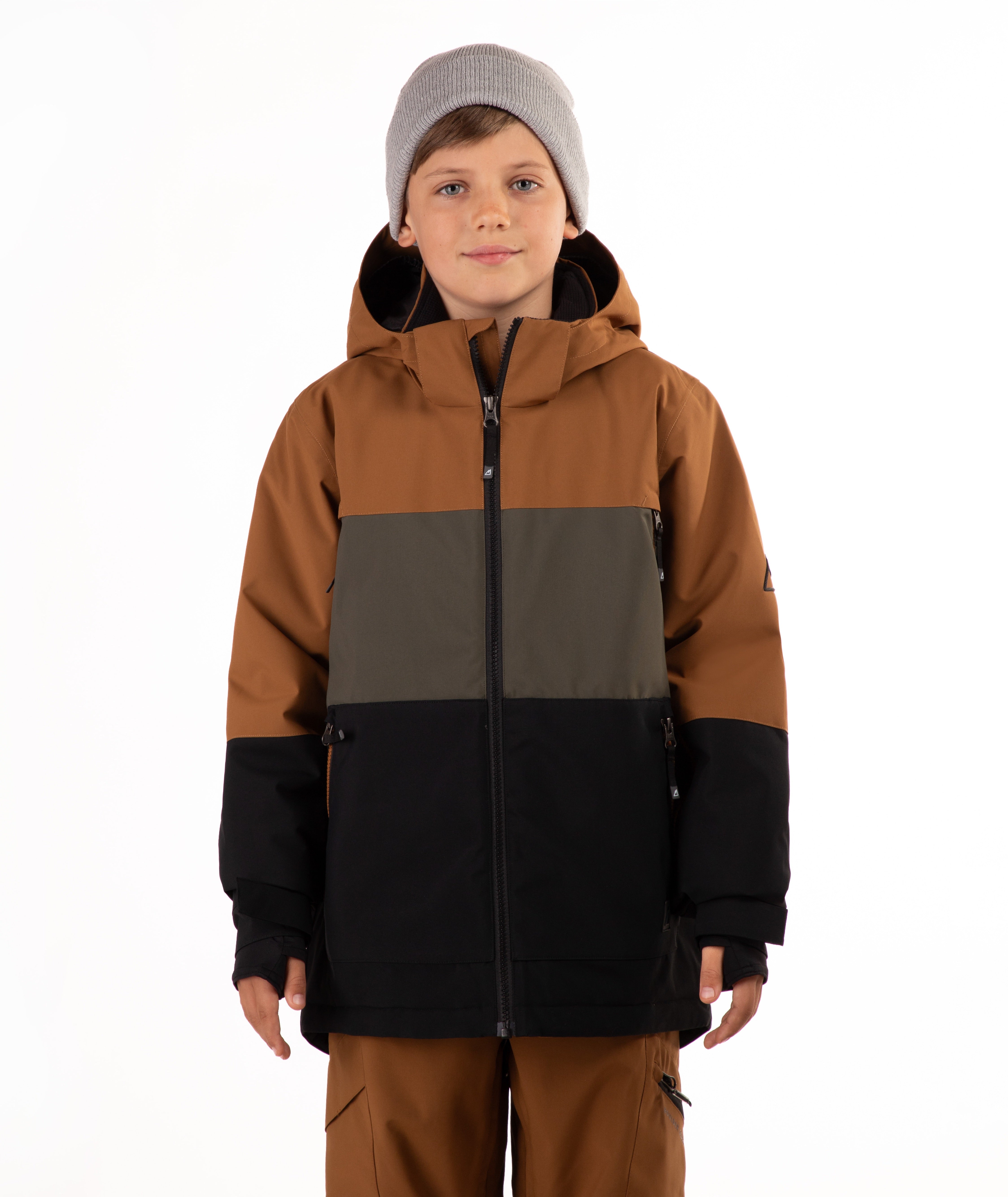 A child wearing a color-blocked ski jacket in brown, green, and black, paired with brown pants and a gray beanie, photographed against a solid white background.