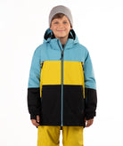 A child wearing a color-blocked ski jacket with light blue, yellow, and black panels, a gray beanie, and yellow ski pants, photographed against a plain white background.