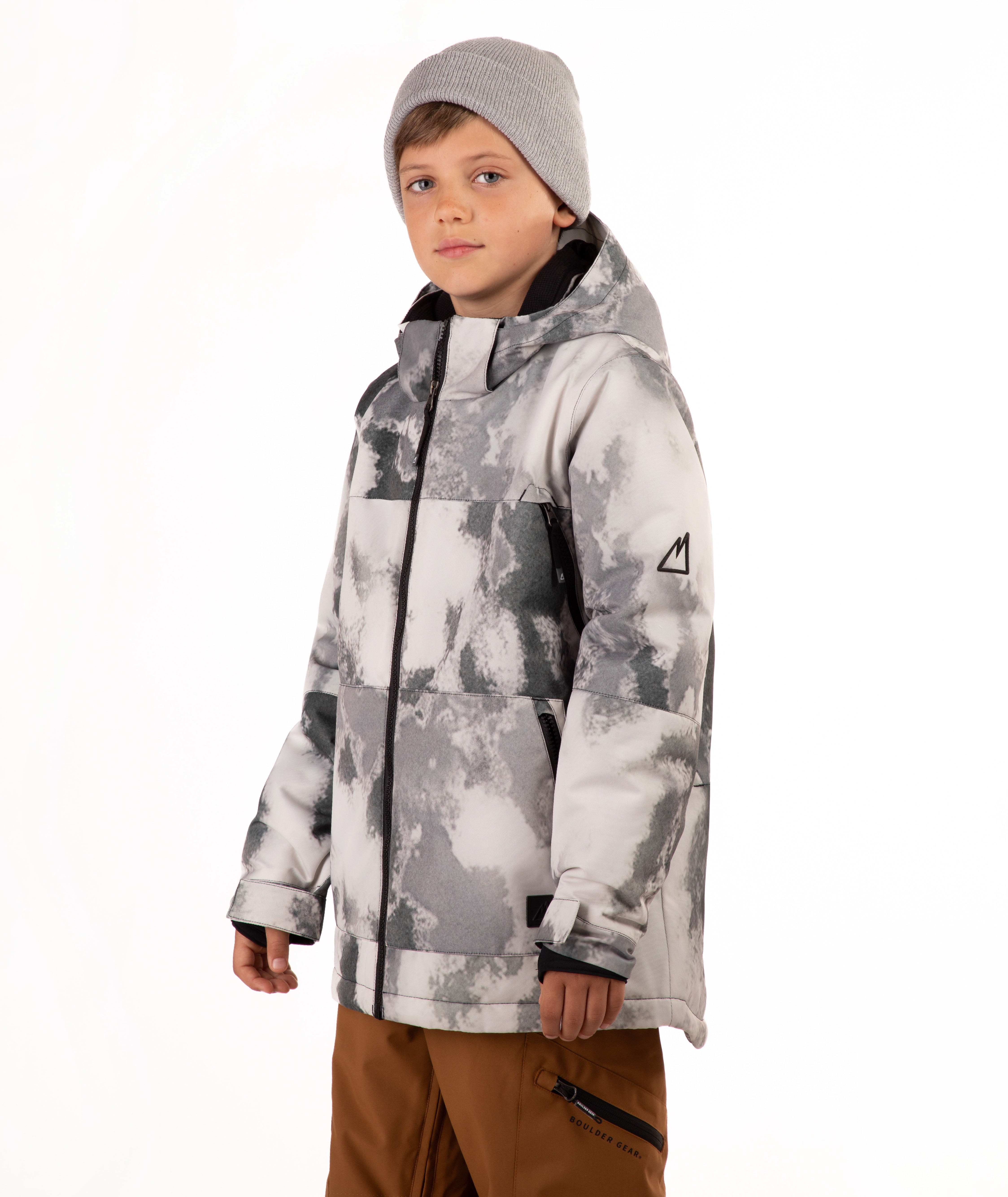 A child wearing a gray and white tie-dye patterned snowboard jacket, a gray beanie, and brown pants, standing against a plain white background.