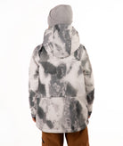 A child wearing a gray and white tie-dye patterned snowboard jacket, a gray beanie, and brown pants, standing against a plain white background.