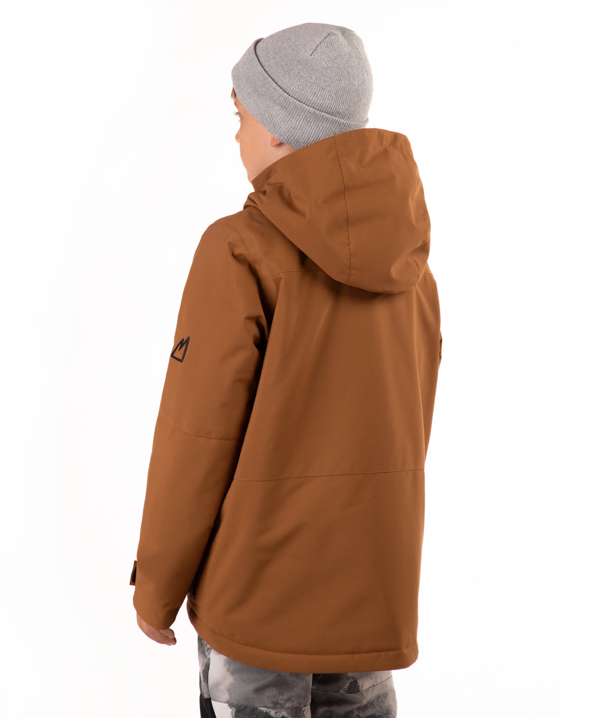 A child wearing a brown hooded snowboard jacket with black zippers, a gray beanie, and patterned pants, standing against a plain white background.