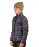 youth boy wearing a multi colored abstract patterned puffer jacket on a white background