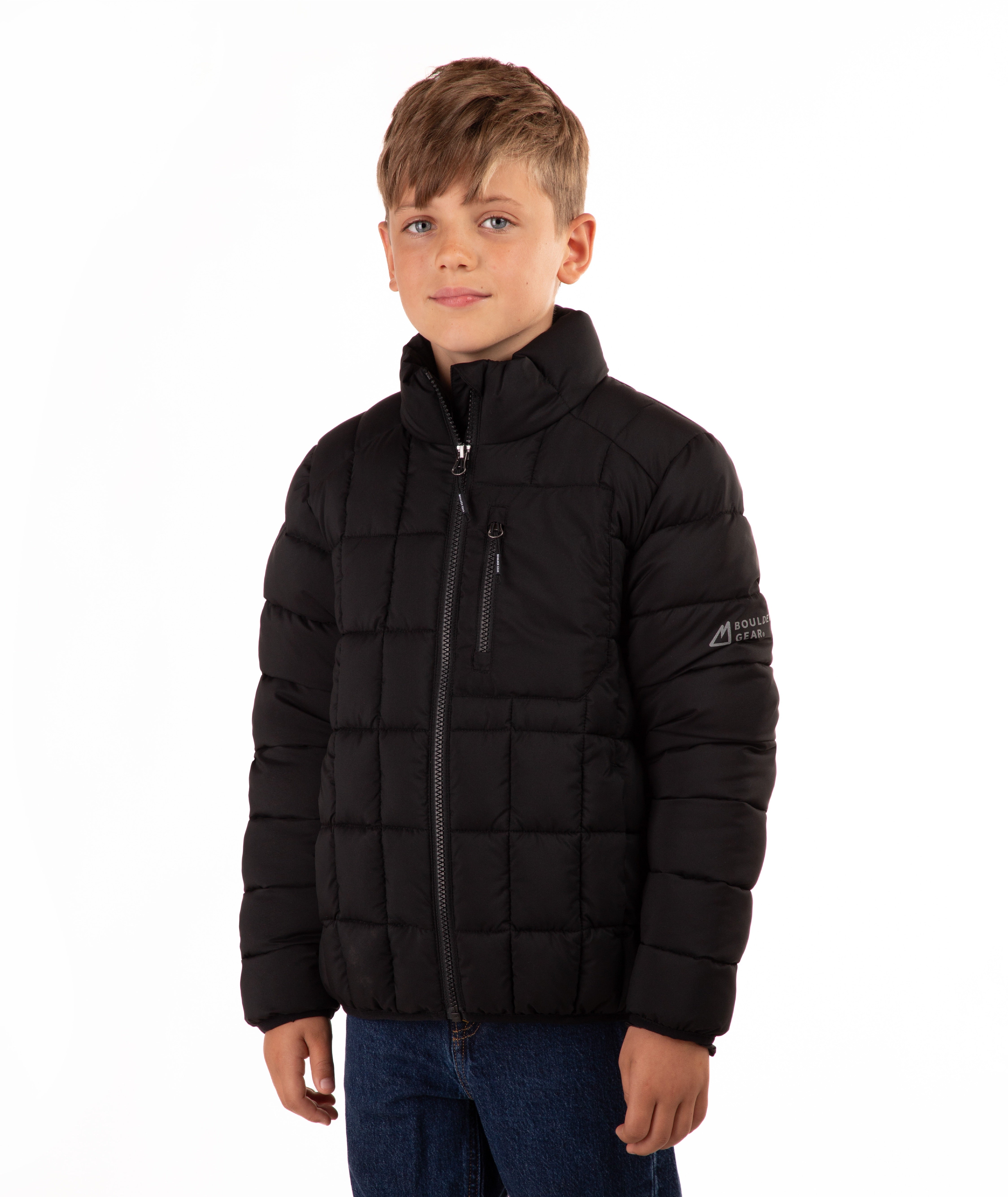 A young boy wearing a black quilted puffer jacket with a stand-up collar and front zipper, paired with blue jeans, photographed against a solid white background.