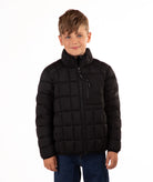 A young boy wearing a black quilted puffer jacket with a stand-up collar and front zipper, paired with blue jeans, photographed against a solid white background.