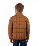 A child viewed from the back wearing a brown quilted puffer jacket and blue jeans against a plain white background.