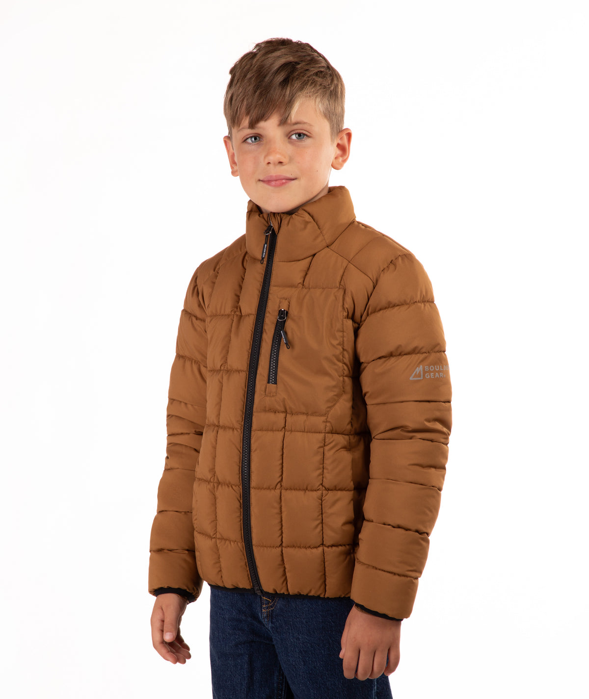 A young boy wearing a brown puffer jacket with black zippers and blue jeans, standing against a plain white background.