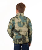 A child viewed from the back wearing a quilted puffer jacket with a blue and green camouflage pattern, paired with blue jeans, against a plain white background.