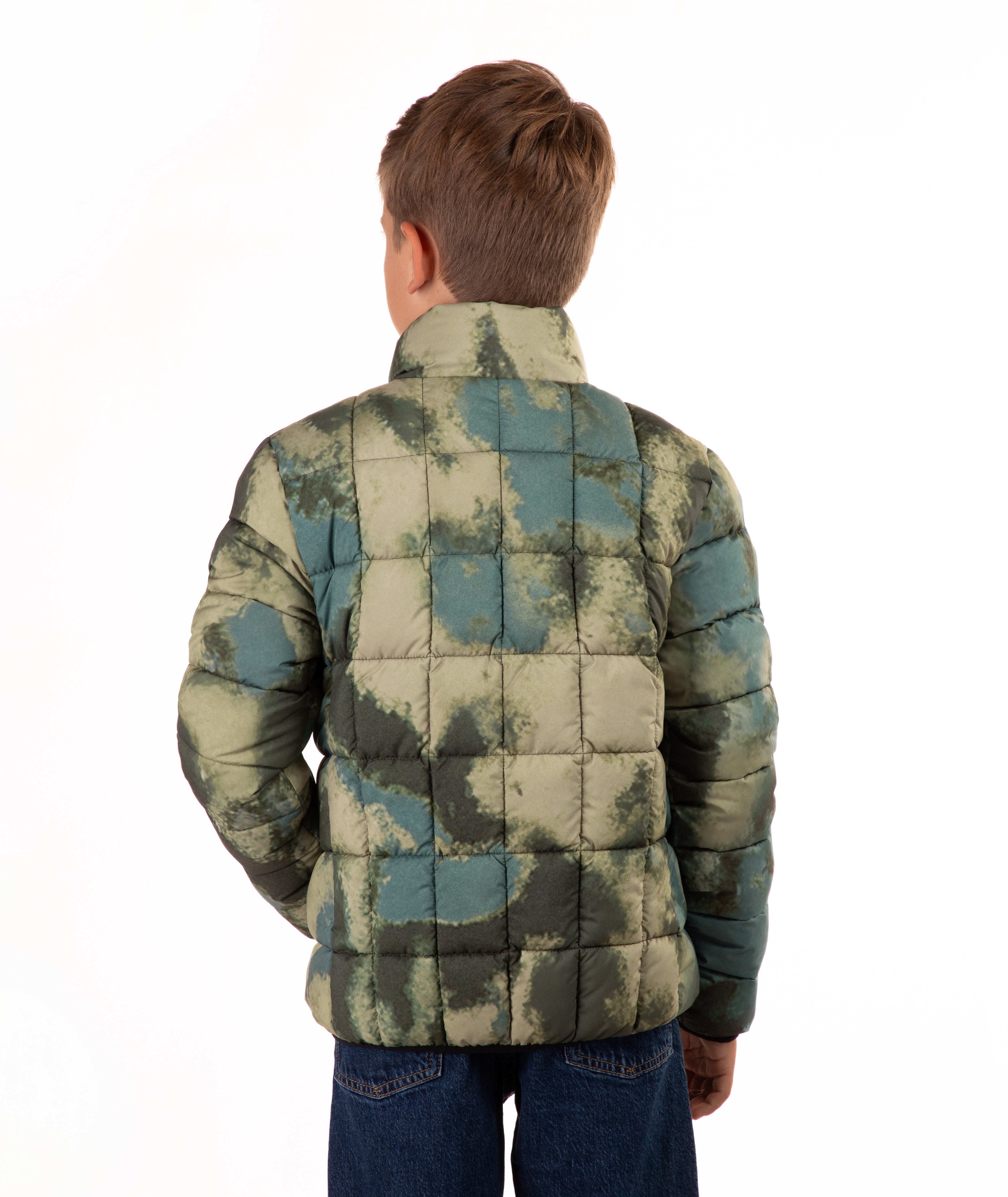 A child viewed from the back wearing a quilted puffer jacket with a blue and green camouflage pattern, paired with blue jeans, against a plain white background.