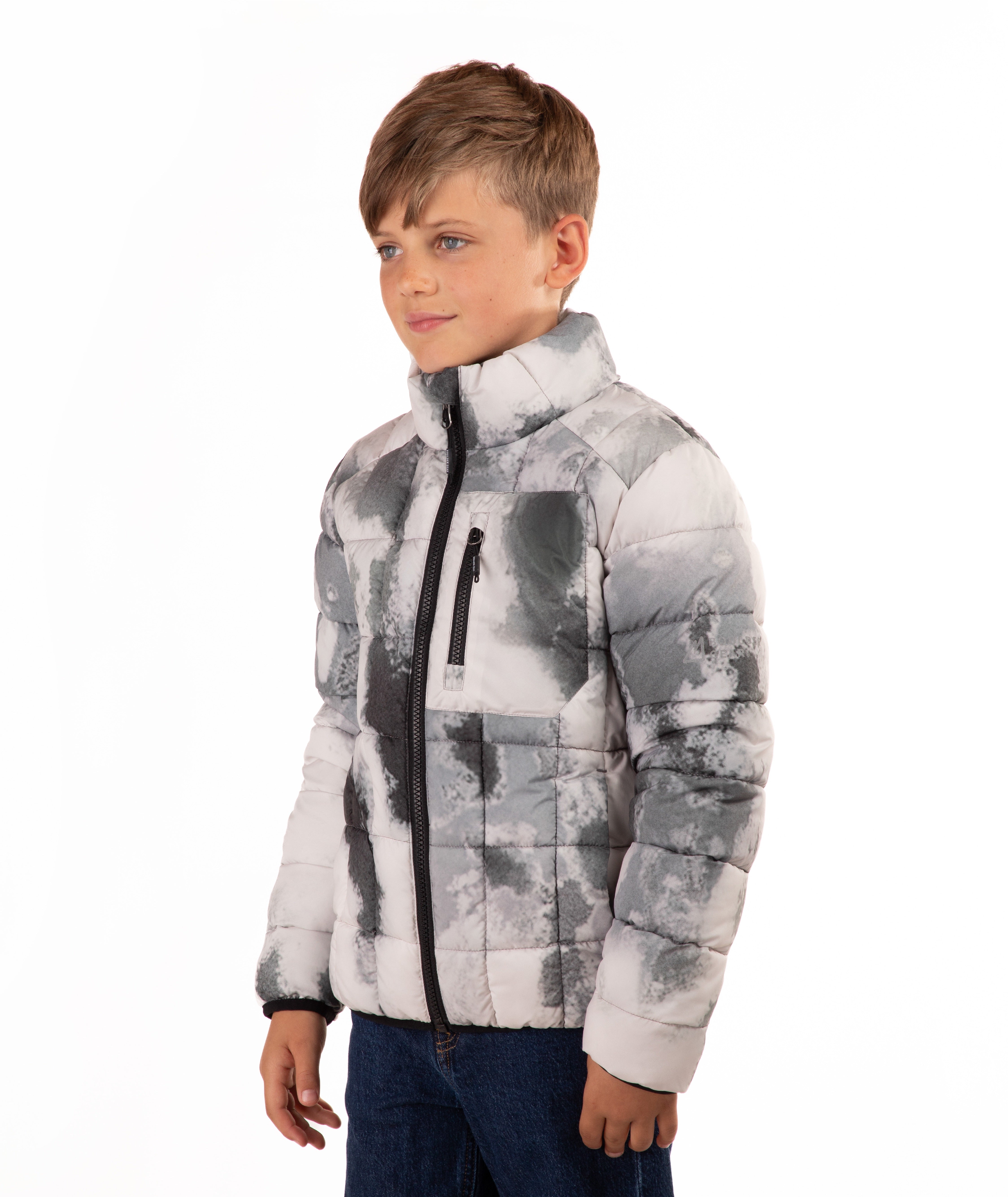 A young boy wearing a gray and white abstract patterned puffer jacket with a black front zipper, paired with blue jeans, photographed against a solid white background.