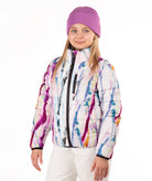 A young girl wearing a white puffer jacket with a colorful paint-splatter pattern, a purple knit beanie, and white pants, photographed against a plain white background.