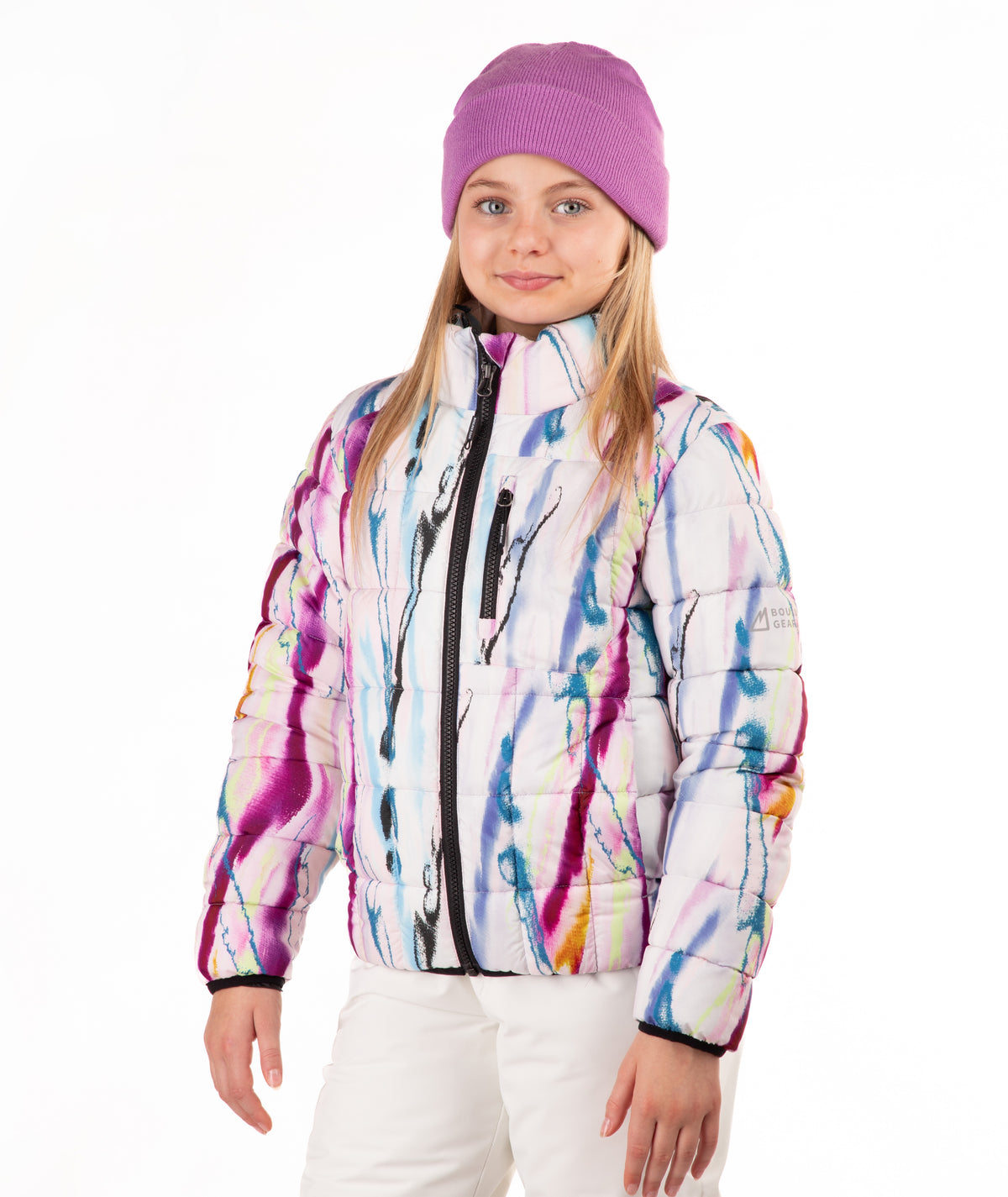 A young girl wearing a white puffer jacket with a colorful paint-splatter pattern, a purple knit beanie, and white pants, photographed against a plain white background.