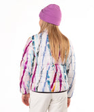A girl shown from the back wearing a white quilted puffer jacket with a colorful paint-splatter pattern in purple, blue, pink, and yellow, paired with a purple knit beanie and white pants, against a plain white background.