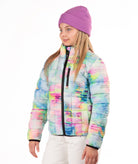A young girl wearing a pastel tie-dye puffer jacket, a purple knit beanie, and white pants, standing against a plain white background.