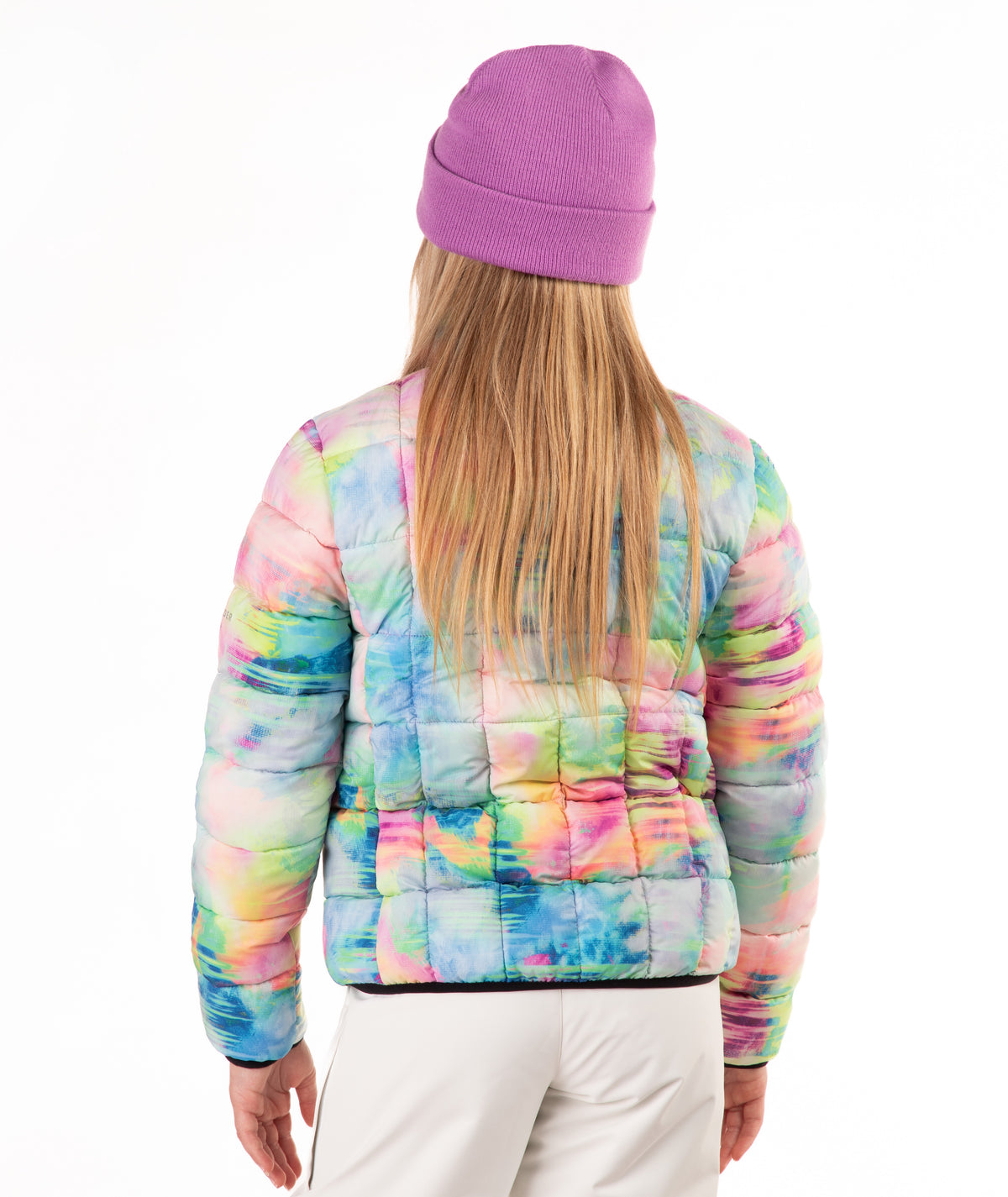 A child wearing a pastel tie-dye puffer jacket, a purple knit beanie, and white pants, shown from the back against a plain white background.