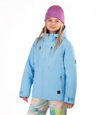 A young girl wearing a light blue ski jacket, a purple knit beanie, and colorful tie-dye snow pants, standing against a solid white background.