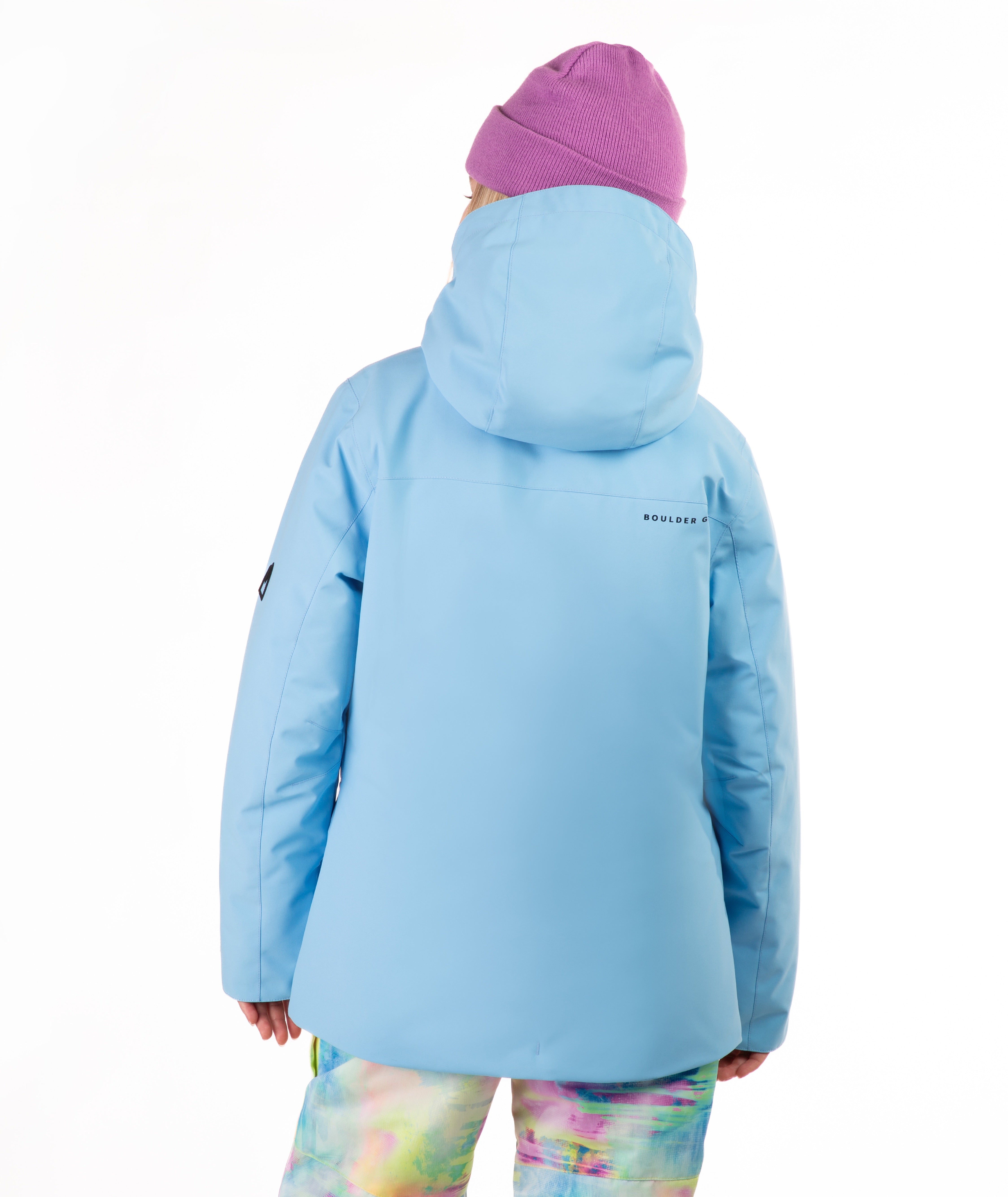 A child shown from the back wearing a light blue hooded ski jacket, a pink knit beanie, and pastel tie-dye pants against a plain white background.