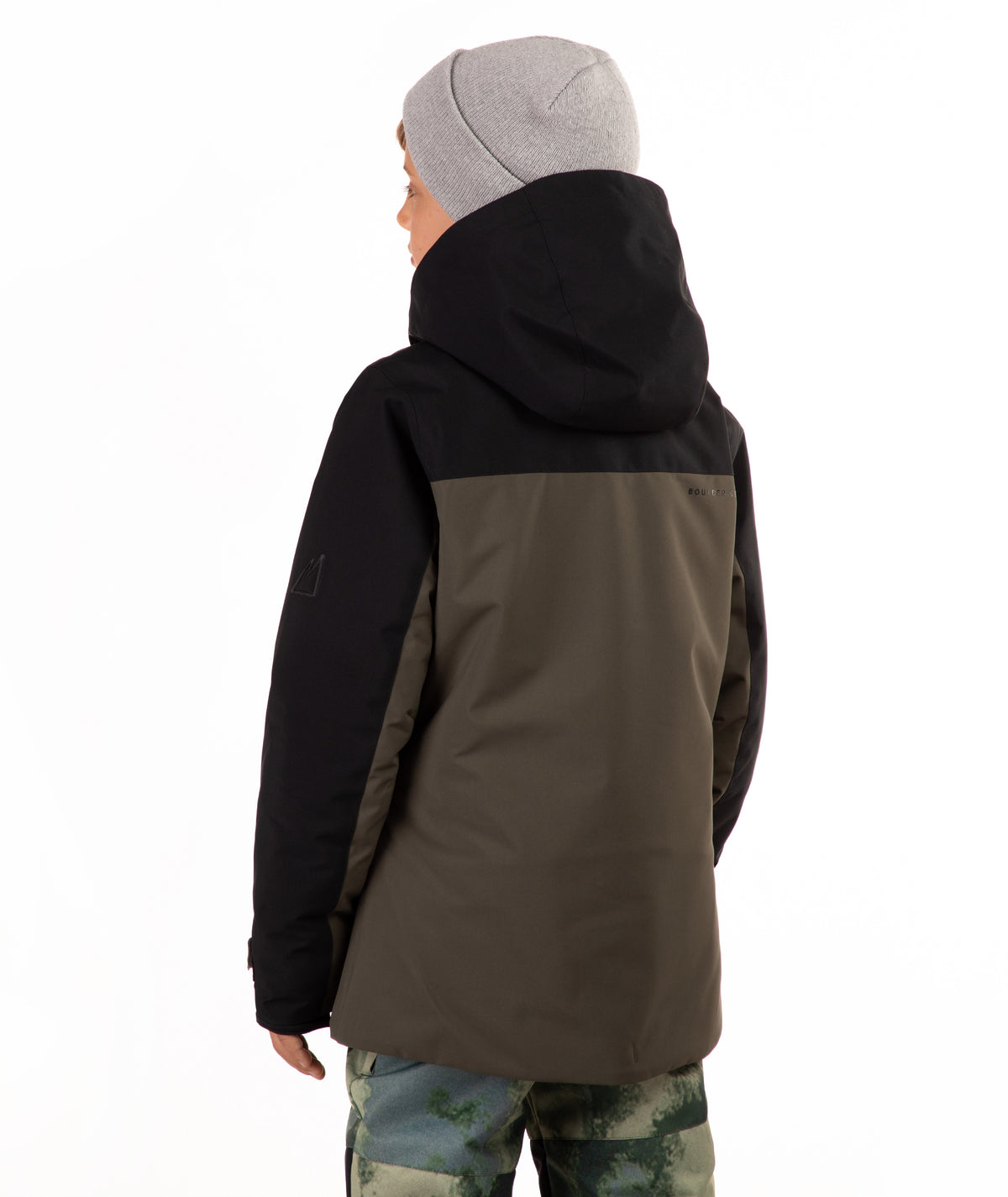 A person shown from the back wearing a color-blocked hooded jacket with a black upper section and sleeves, and an olive-brown lower section, paired with a light gray beanie and camouflage pants, against a plain white background.