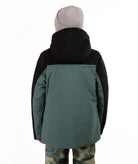 A child viewed from the back wearing a color-blocked ski jacket in black and muted teal, paired with a gray beanie and camouflage-patterned pants, against a plain white background.