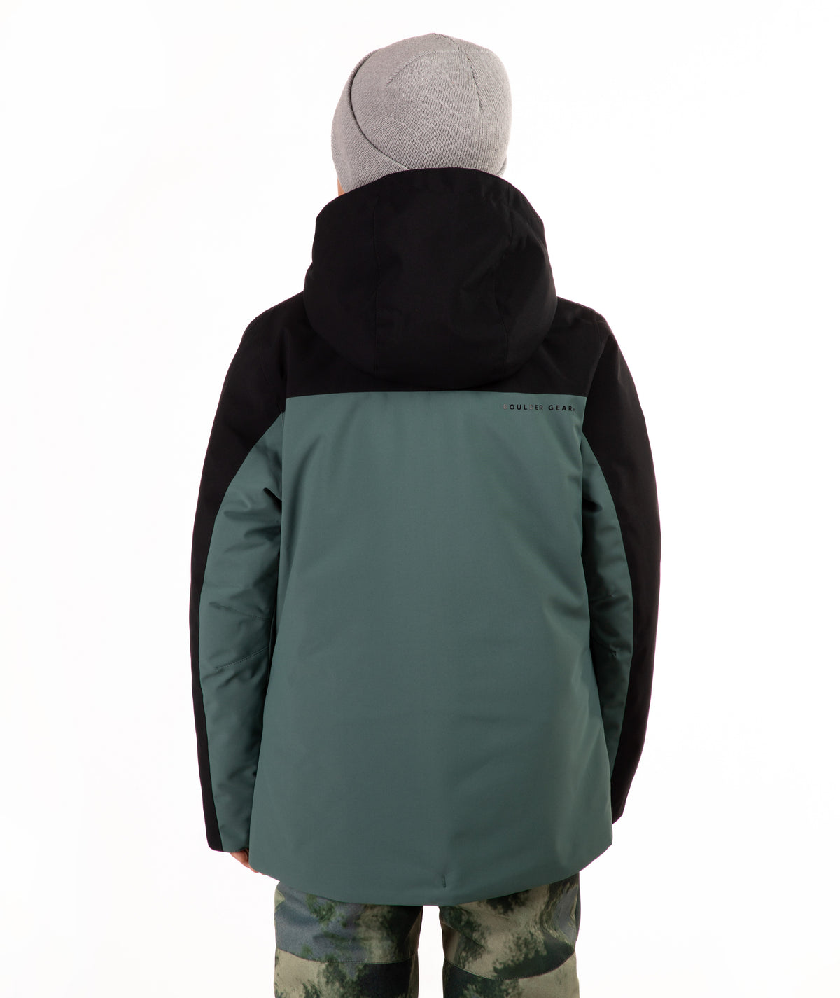 A child viewed from the back wearing a color-blocked ski jacket in black and muted teal, paired with a gray beanie and camouflage-patterned pants, against a plain white background.