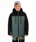 A child wearing a color-blocked ski jacket in black and muted teal, paired with a gray beanie and camouflage-patterned pants, against a plain white background.