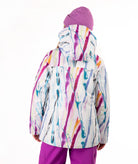 A child viewed from the back wearing a hooded ski jacket with a colorful abstract paint-stroke pattern in pink, purple, blue, yellow, and orange on a white base, paired with a purple beanie and purple pants, against a plain white background.