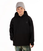 A child wearing a black pullover hoodie with a small tonal square logo patch on the left chest, paired with a light gray knit beanie and camouflage-patterned pants, photographed against a plain white background.