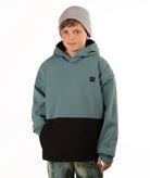 A child wearing a color-blocked pullover hoodie with a muted teal green upper section and a black lower section, paired with a light gray beanie and camouflage-patterned pants, against a plain white background.